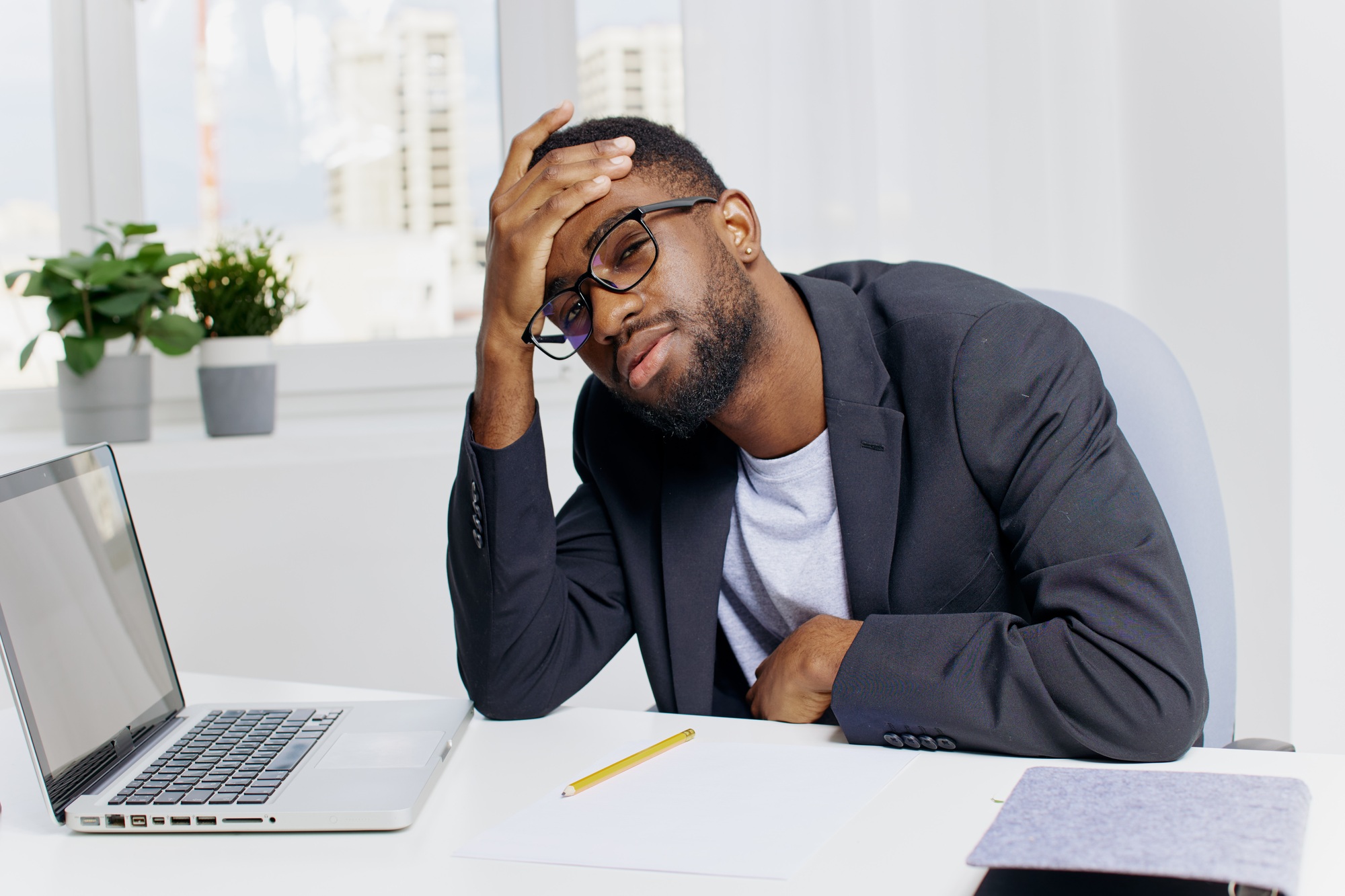 Stressed businessman in office suit sitting at desk with head in hands surrounded by papers and